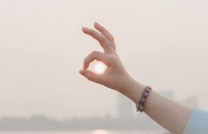 A hand creating an OK sign as the sun sets in the background, capturing a warm and serene atmosphere.